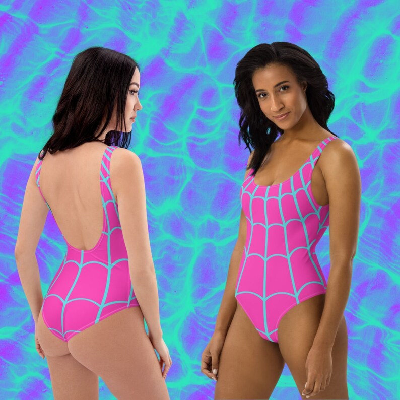May include: A one-piece swimsuit featuring a vibrant pink base colour with a repeating light blue spider web pattern. The garment has a scoop neckline, wide shoulder straps, and a high-cut leg design, shown from both the front and back views.