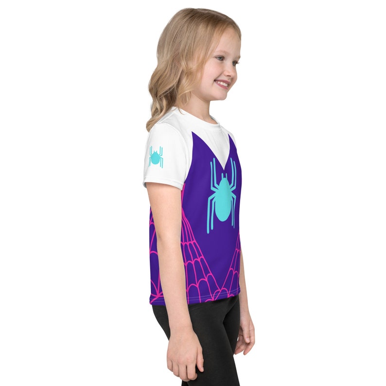 K&ouml;nnte beinhalten: Ein wei&szlig;es T-Shirt mit einem violetten Spinnennetz-Design und einer blauen Spinne in der Mitte. Das Spinnennetz ist rosa und wei&szlig;.