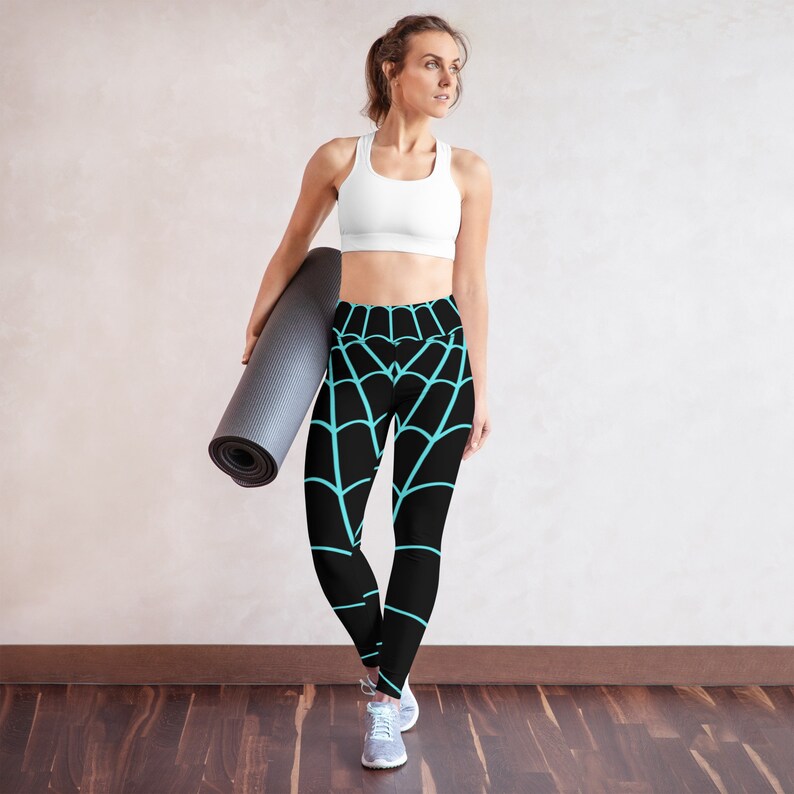 May include: Black yoga pants with a blue spiderweb pattern. The pants are high-waisted and have a fitted silhouette. A woman is wearing the pants and holding a black yoga mat.