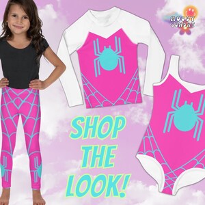 Op de afbeelding: Een roze en blauwe outfit voor kinderen met een spinnenweb-thema. De outfit bestaat uit een shirt met lange mouwen, leggings en een badpak. Het shirt heeft een witte lange mouw en een roze voorkant met een blauwe spin-afbeelding. De leggings zijn roze met een blauw spinnenweb-ontwerp. Het badpak is roze met een blauwe spin-afbeelding en een witte rand. De tekst "SHOP THE LOOK!" is geschreven in groen en blauw.