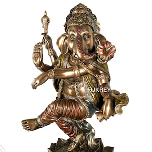 Könnte beinhalten: Bronzefarbene Statue der hinduistischen Gottheit Ganesha, dargestellt beim Tanzen auf einer Lotusblütenbasis. Die Statue weist aufwendige Details auf, darunter mehrere Arme, aufwendiger Schmuck und ein dekorativer Kopfschmuck. Der Text "Fukrey Hast Kala Kendra" ist sichtbar.