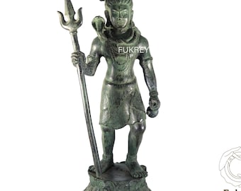 May include: A bronze-colored statue of a standing deity holding a trident and a small object. The statue has intricate details and is mounted on a decorative base. The text "Fukrey Hast Kala Kendra" is visible.