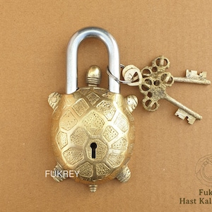 May include: A brass turtle-shaped padlock with a silver shackle and ornate keys. The padlock has a textured shell design and the word "Fukrey" is visible. The keys are attached to the padlock with a metal ring.