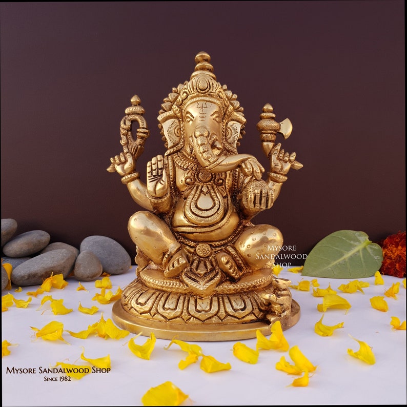 K&ouml;nnte beinhalten: Eine goldfarbene Messingstatue von Ganesha, dem hinduistischen Gott der Weisheit und des Wohlstands, der auf einem Lotusthron sitzt. Die Statue ist aufwendig detailliert und zeigt Ganeshas charakteristische Elefantenkopf, R&uuml;ssel und vier Arme.