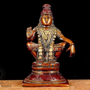 Puede incluir: Una estatua de bronce de una figura sentada con detalles intrincados. La figura está adornada con joyas ornamentadas y un tocado. La estatua está montada sobre una base decorativa. El texto "Fukrey Hast Kala Kendra" es visible.