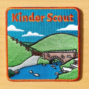 May include: An embroidered patch featuring a blue sky, green hills, a stone bridge over a blue river, and the text "Kinder Scout" in orange.
