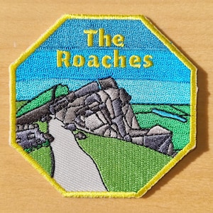 May include: A yellow octagon-shaped embroidered patch with a blue sky background and a green grassy foreground. The patch features a grey rock formation with the text "The Roches" in yellow lettering.