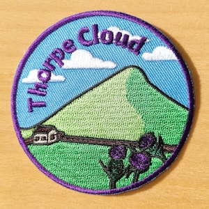 May include: Purple and blue embroidered patch featuring the text "Thorpe Cloud" and an image of a green hill with a small house and purple flowers.
