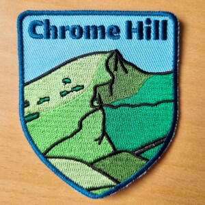 May include: A blue and green embroidered patch with the text "Chrome Hill" in white. The patch depicts a stylised green hill with a blue sky.