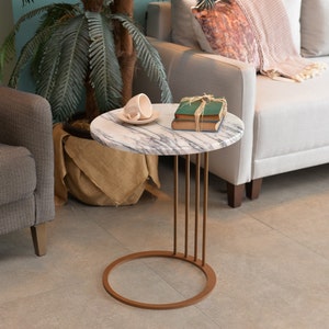 May include: A round side table with a white marble top and a gold metal base with a ring design. The table has a cup and saucer and a stack of books on top.