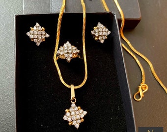 May include: A gold-toned jewelry set featuring a pendant, ring, and earrings, all with a starburst design of small, clear stones. The set is displayed in a black box, with a gold chain necklace. The jewelry is likely made of gold-plated metal.