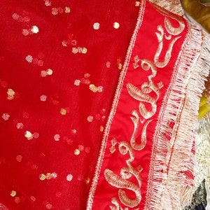 May include: Red sheer fabric with gold sequins and a red border with gold embroidery. The embroidery features a repeating pattern of a stylized flower.
