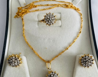 May include: A gold necklace, ring, and earrings set with a delicate chain and a round pendant and earrings with a cluster of small white stones.