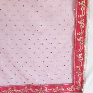 May include: A sheer pink fabric with gold polka dots and a red border with gold embroidery. The embroidery features a repeating pattern of stylized floral designs.