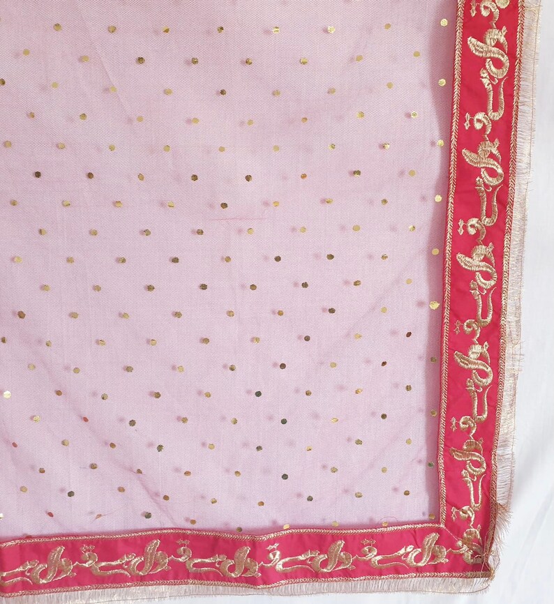 May include: A sheer pink fabric with gold polka dots and a red border with gold embroidery. The embroidery features a repeating pattern of stylized floral designs.