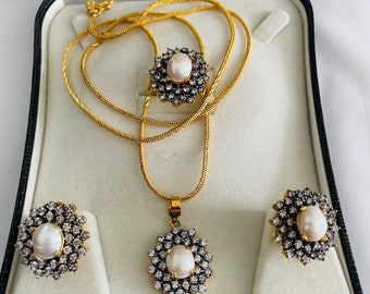 May include: A gold necklace with a pearl and diamond pendant, a pair of matching pearl and diamond earrings, and a gold chain in a white box.