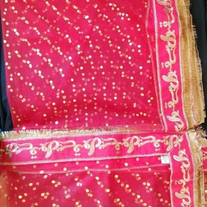 May include: Red sheer fabric with gold sequins and a gold embroidered border. The border features a repeating pattern of stylized Arabic script.