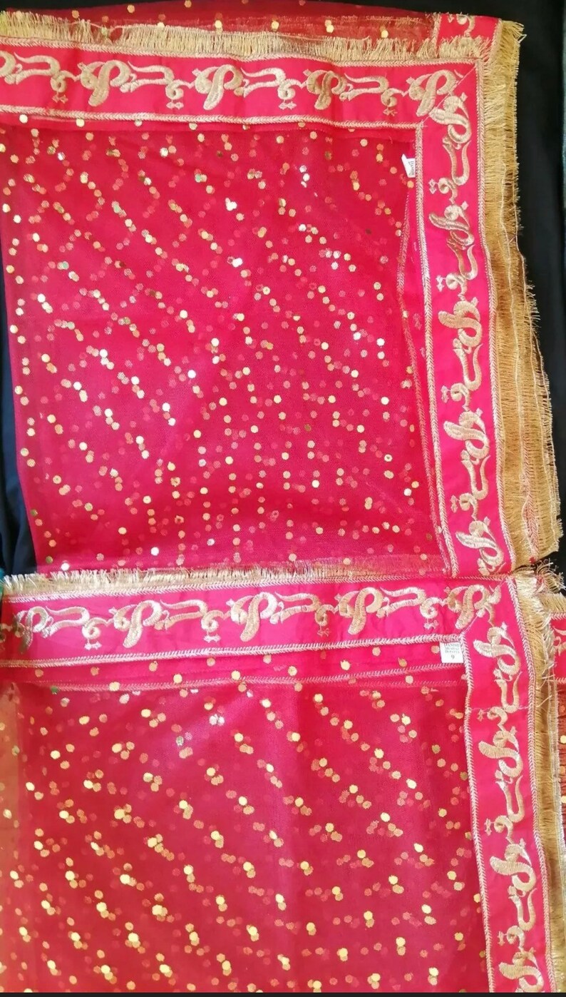 May include: Red sheer fabric with gold sequins and a gold embroidered border. The border features a repeating pattern of stylized Arabic script.