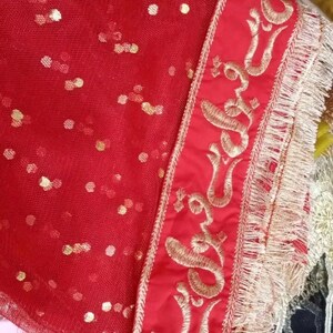 May include: Red sheer fabric with gold sequins and a gold embroidered border. The border features a repeating pattern of a stylized flower.