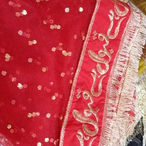 May include: Red sheer fabric with gold sequins and a gold embroidered border. The border features a repeating pattern of a stylized symbol.