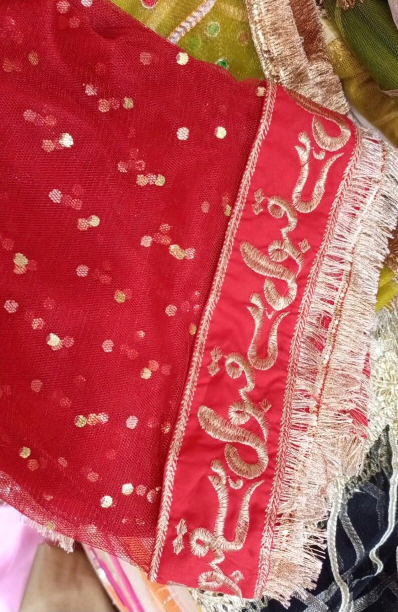 May include: Red sheer fabric with gold sequins and a gold embroidered border. The border features a repeating pattern of a stylized symbol.