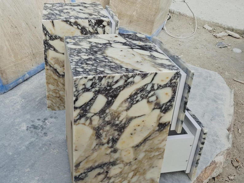 May include: Two rectangular pedestals featuring a polished marble surface with a high-contrast pattern of cream, white, and dark charcoal-black veining. Each unit has a smooth, block-like structure with a visible white interior drawer component.