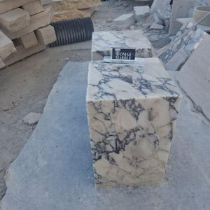 Puede incluir: Dos pedestales de m&aacute;rmol con un patr&oacute;n veteado blanco y gris. Los pedestales son rectangulares y tienen el texto "TOMAS MARBLE" en un peque&ntilde;o letrero. Los pedestales est&aacute;n sobre una gran losa de piedra gris.