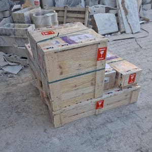 May include: A wooden shipping crate secured with plastic straps and clear shrink wrap, featuring red and white fragile labels with a wine glass icon. The crate is constructed from light-coloured pine planks and sits on a matching wooden pallet base.