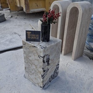 Pu&ograve; includere: Un piedistallo in marmo bianco con venature nere, con un vaso nero con bacche rosse. Il piedistallo &egrave; etichettato "Thomas Marble".