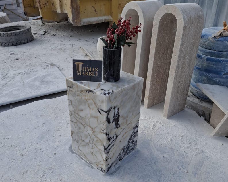 Pu&ograve; includere: Un piedistallo in marmo bianco con venature nere, con un vaso nero con bacche rosse. Il piedistallo &egrave; etichettato "Thomas Marble".