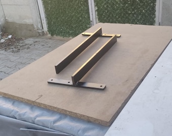 May include: Two black metal brackets are attached to a light brown piece of wood. The brackets are shaped like an L and have a flat surface on the top.
