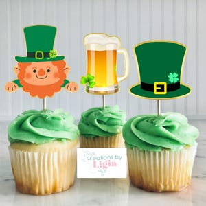Puede incluir: Tres cupcakes con glaseado verde y adornos temáticos del Día de San Patricio. Los adornos incluyen un duende, una jarra de cerveza y un sombrero verde con un trébol. Los cupcakes están en moldes de papel blancos.
