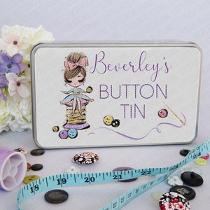 May include: A white metal tin with a colourful illustration of a girl sitting on a spool of thread. The tin has the text "Beverley's Button Tin" printed on it.