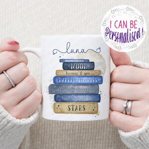 May include: White ceramic mug with a blue and gold design featuring a stack of books with the words "Make sure to aim for the moon because if you happen to miss you will always land amongst the stars". The mug has the name "aluna" written on it in a cursive font.