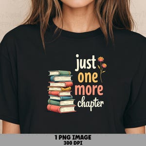 May include: A black t-shirt featuring a graphic of a stack of colorful books with the text "just one more chapter" in a multi-colored font, accompanied by a small illustration of two orange flowers on thin green stems to the right of the text.