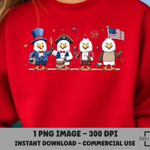 May include: A red sweatshirt featuring a cartoon illustration of four patriotic eagles. Each eagle is dressed in festive attire, holding items like a drum, a flag, and a torch, with fireworks in the background. The design is perfect for celebrating Independence Day.