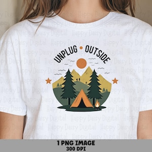 May include: A white t-shirt featuring a graphic print of a camping scene with a tent, a campfire, pine trees, and mountains under a sun. The text "UNPLUG OUTSIDE" is arched above the illustration, which is flanked by two small orange stars.