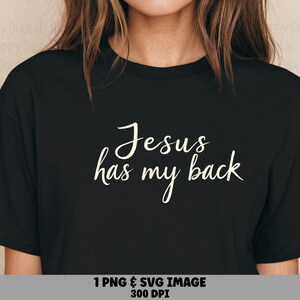 May include: A black short-sleeved t-shirt featuring the white text "Jesus has my back" printed in a cursive script font across the center of the chest. The shirt has a crew neckline and a standard fit, showcasing the graphic design clearly.