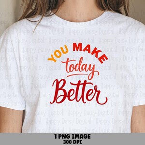Puede incluir: Una camiseta blanca de manga corta con el texto YOU MAKE today Better impreso en la parte delantera. La palabra YOU es de color naranja, mientras que las palabras MAKE, today y Better son rojas, usando una mezcla de tipografía de bloque y cursiva.