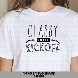 May include: A white short-sleeved t-shirt featuring black text that reads "CLASSY UNTIL KICKOFF" with a graphic of football laces centered between the words "UNTIL" and "KICKOFF" on the front of the garment.
