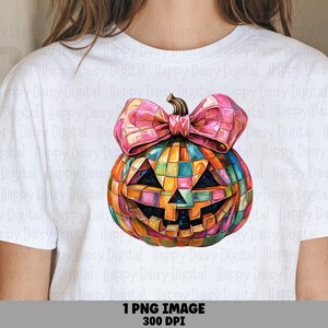 Op de afbeelding: Een wit t-shirt met een afbeelding van een Halloween-pompoen met een veelkleurig mozaïekpatroon. De pompoen heeft een grote roze strik aan de bovenkant en een uitgesneden gezicht met driehoekige ogen en een gekartelde mond. Tekst: 1 PNG IMAGE 300 DPI.