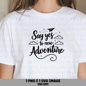 Puede incluir: Una camiseta blanca de manga corta con el texto negro "Say yes to new Adventure" junto a ilustraciones gráficas de un avión de papel, nubes y pequeñas estrellas. El diseño está centrado en el pecho de la prenda.