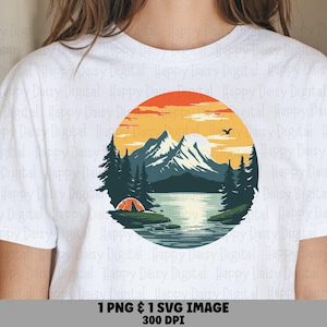 May include: A white t-shirt featuring a circular graphic of a mountain landscape at sunset. The design includes dark green pine trees, a calm lake, a small orange tent, and snow-capped mountains against a yellow and orange sky with a bird.