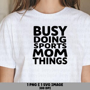 Może przedstawiać: Biały t-shirt z krótkim rękawem z pogrubionym czarnym napisem na środku klatki piersiowej o treści BUSY DOING SPORTS MOM THINGS. Koszulka ma klasyczny okrągły dekolt i standardowy krój, zapewniając schludny wygląd do codziennego noszenia.