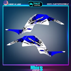 May include: Blue and white graphic design for a Raptor ATV. The design features a black and white distressed pattern, the word "Raptor" in white, and the Bridgestone logo.