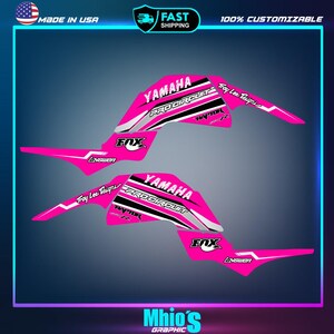 May include: Pink and white Yamaha Pro Circuit ATV graphics kit with Fox Racing and Troy Lee Designs logos.