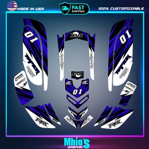 May include: A set of blue, white, and black graphic decals for a Yamaha Raptor motorcycle. The decals feature the words "Raptor" and "Motocross", the number "01", and the brand names "Fox" and "Dunlop".