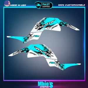 K&ouml;nnte beinhalten: Zwei blaue und wei&szlig;e Grafikdesigns f&uuml;r ein Yamaha Raptor ATV. Die Designs zeigen das Wort "Raptor" in Schwarz und Wei&szlig; mit einem blauen und schwarzen abstrakten Design. Die Designs beinhalten auch die W&ouml;rter "Bridgestone" und "ASV".