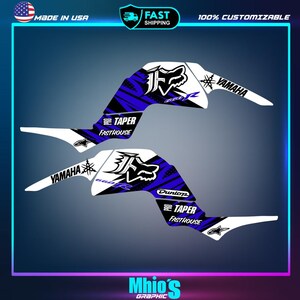 May include: A set of two Yamaha motorcycle graphics featuring a blue and white colour scheme with a fox head logo, "Pro Taper FastHouse" text, and "Dunlop" text.
