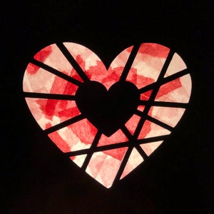 May include: A red heart-shaped paper lantern with a delicate, intricate design. The lantern is illuminated from behind, creating a warm glow.